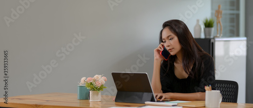 Female professor talking to her student on the phone while working on digital tablet in living room