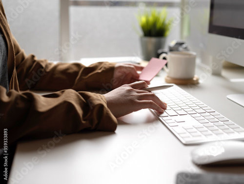 Female working with computer device while looking an idea on notepad on white office desk