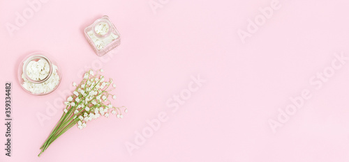 Small first spring flowers lilies of the valley and beautiful glass bottle with dried petals for aromatherapy. Spring or spa banner with space for text. Creative flat lay composition with copy space.