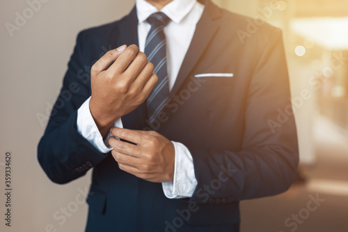 Obraz na plátně businessman wearing business suit fasten cufflink or button on sleeve of classic jacket and factory background