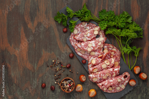 Smoked sausage salami with hazelnuts in a wooden plate on the table. Top view photo