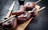 Barbecue dry aged wagyu Brazilian picanha from the sirloin cap of rump beef offered as closeup on a skewer on a wooden board on black background with copy space right