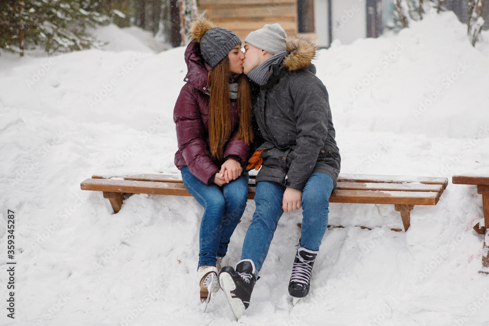 Young guy and a girl are kissing in a winter park. - obrazy, fototapety, plakaty 