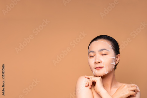 Portrait of Asian woman with facial mask standing isolated on beige background.