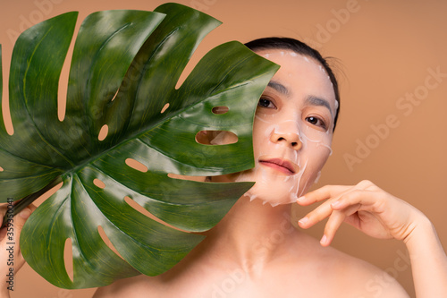 Portrait of Asian woman with facial mask standing isolated on beige background.