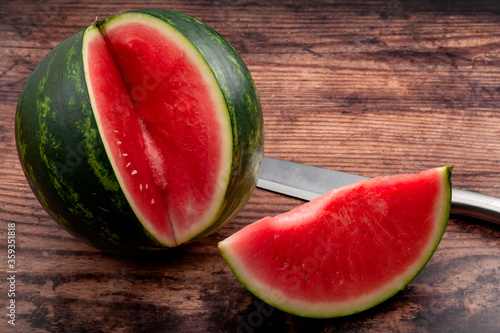 Vitamin rich fruits and summertime refreshment concept with photograph of perfect seedless watermelon slice and metal knife isolated on rustic wood background