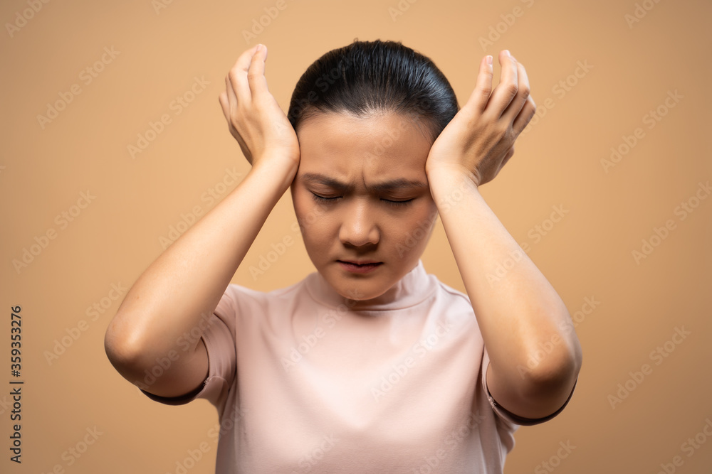 Asian woman was sick with headache standing isolated on beige background. Asian woman was sick with headache standing isolated on beige background.