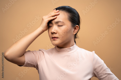 Asian woman was sick with headache standing isolated on beige background.