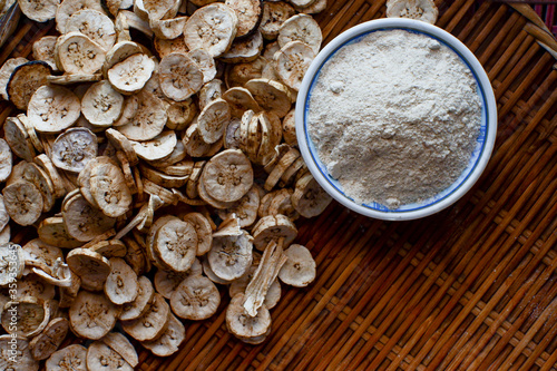 Dried banana slices  With raw banana powder in a cup  Raw banana powder is an ancient medicine used for gastritis treatment.  All laid on a wooden floor