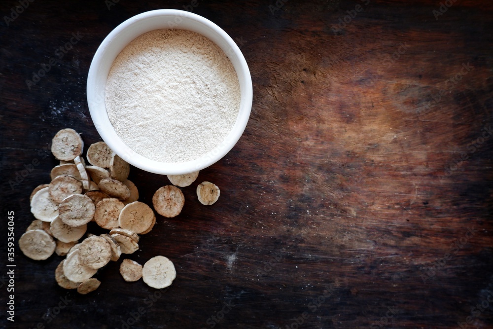 Fototapeta premium Dried banana slices With raw banana powder in a cup Raw banana powder is an ancient medicine used for gastritis treatment. All laid on a wooden floor
