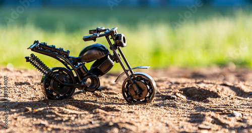 Fototapeta Naklejka Na Ścianę i Meble -  Home-made metal model - a sports motorcycle toy stands on a sand mountain on an abstract green background