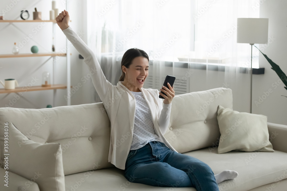 Excited girl sit on sofa hold cell enjoy great news celebrate university admission sms scholarship approval scream with joy raise fist feels happy, new apps, offer sale discount notification concept Excited girl sit on sofa hold cell enjoy great news celebrate university admission sms scholarship approval scream with joy raise fist feels happy, new apps, offer sale discount notification concept