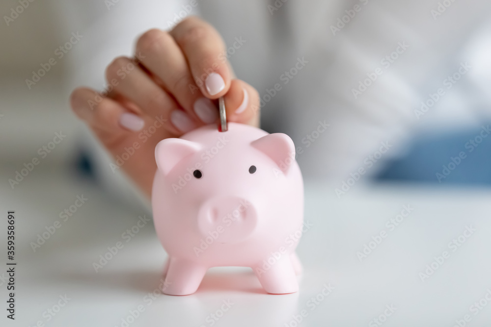 Close up image female fingers puts coin inside of piggy bank. Save money, think about future, avoid unnecessary expenses, housewife manage control family household budget, economy cost savings concept Close up image female fingers puts coin inside of piggy bank. Save money, think about future, avoid unnecessary expenses, housewife manage control family household budget, economy cost savings concept