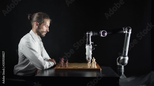 Modern technology, man playing chess with a robot, the confrontation between man and artificial intelligence, futuristic robotic arm participates in the game.