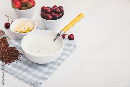 Bowl of yogurt with fruits and flax seeds on white table