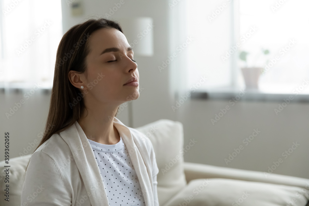 Calm serene woman resting sitting on couch in modern living room closed her eyes breath fresh humidified air. Fatigue relief repose, boost inner balance and mindfulness, meditation practice concept Calm serene woman resting sitting on couch in modern living room closed her eyes breath fresh humidified air. Fatigue relief repose, boost inner balance and mindfulness, meditation practice concept
