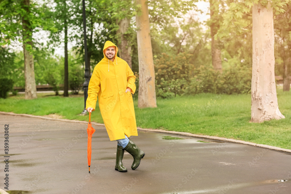 Fototapeta premium Young man with umbrella wearing raincoat outdoors