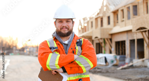 Caucasian foreman in orange workwear holding notebook on construction site.