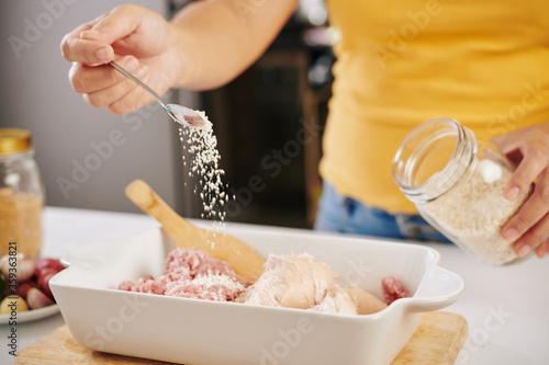Woman putting some spoons of bread crumps into the bowl with ground beef