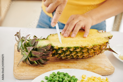 Close-up image of woman cutting fresh ripe pineaaple with sharp ceramic knife photo