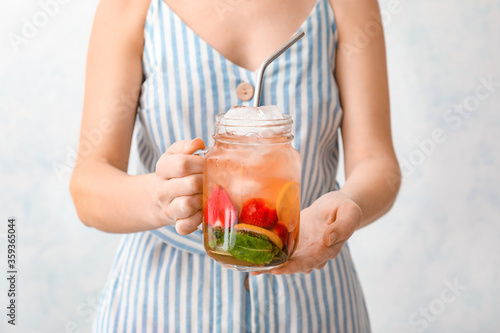 Woman holding mason jar of fresh strawberry lemonade on light background