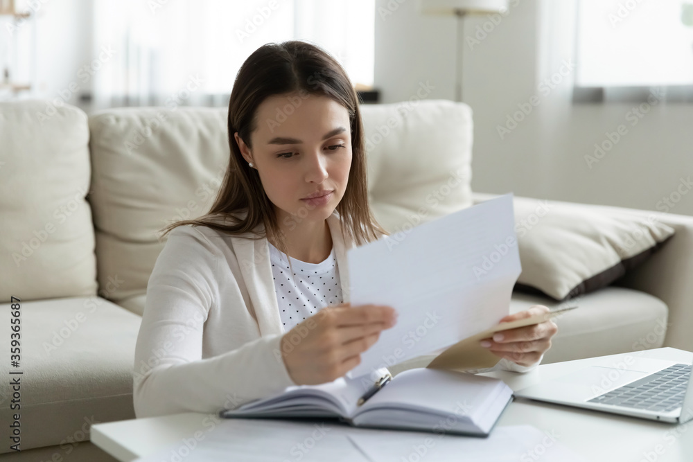 Woman sit at coffee table at home holding paper read personal touching letter from friend or relative looking like she missed or upset by sad news, frustrated female received postal message concept Woman sit at coffee table at home holding paper read personal touching letter from friend or relative looking like she missed or upset by sad news, frustrated female received postal message concept