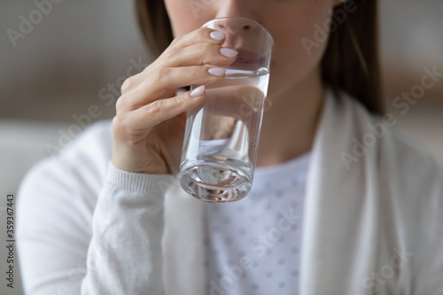 Close up image woman sit indoors holds glass of still or mineral water drinking clean aqua reducing thirst. Healthy lifestyle life habits, enough quantity every day for beauty skin health care concept photo