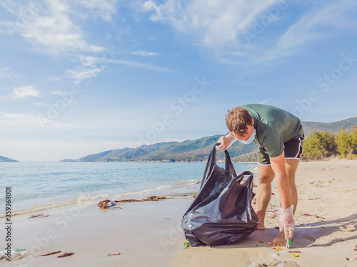Man in gloves pick up plastic that pollute sea and forest. Problem of spilled rubbish trash garbage on the beach sand caused by man-made pollution, campaign to clean volunteer in concept © NOVOZHILOV ANDREI
