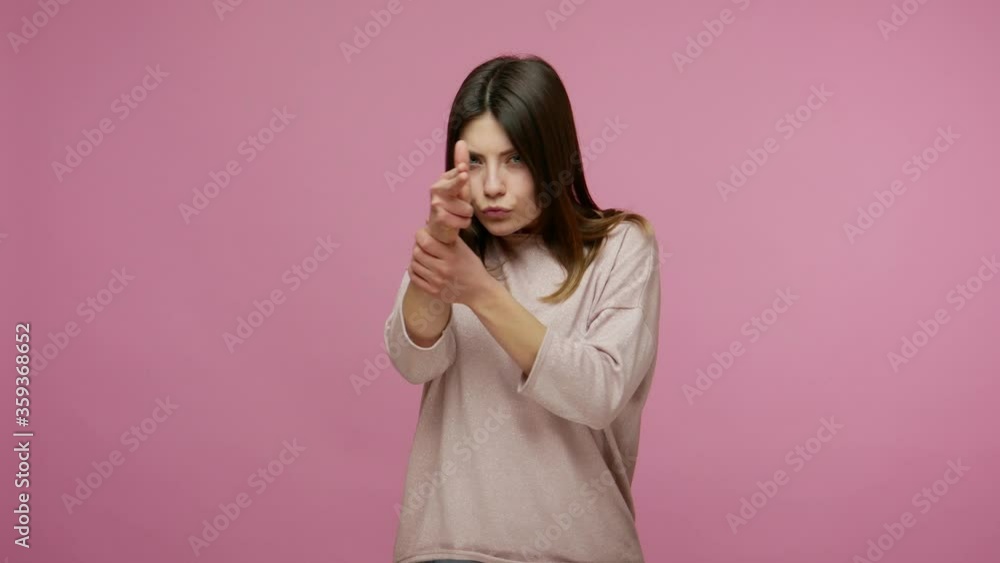 Brunette woman pointing finger gun, threatening to murder, looking around for target and shooting, killing with hand pistol, showing direction to camera. indoor studio shot isolated on pink background Brunette woman pointing finger gun, threatening to murder, looking around for target and shooting, killing with hand pistol, showing direction to camera. indoor studio shot isolated on pink background