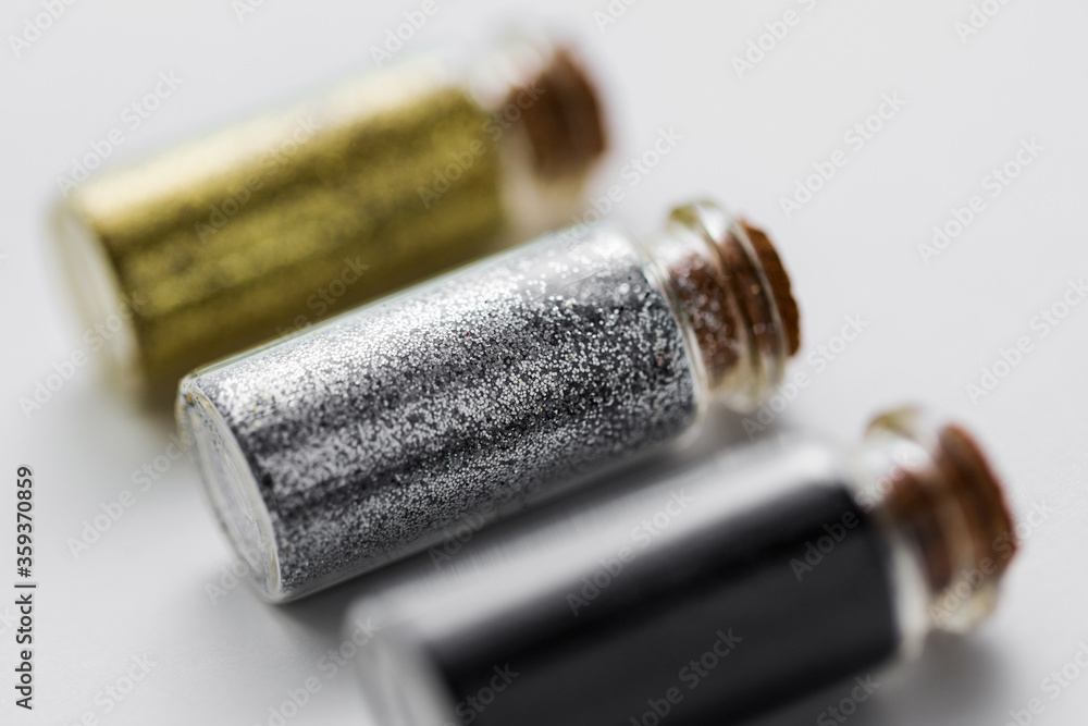 party, decoration and holidays concept - close up of gold, silver and black metallic glitters in small glass bottles with cork stoppers over white background party, decoration and holidays concept - close up of gold, silver and black metallic glitters in small glass bottles with cork stoppers over white background