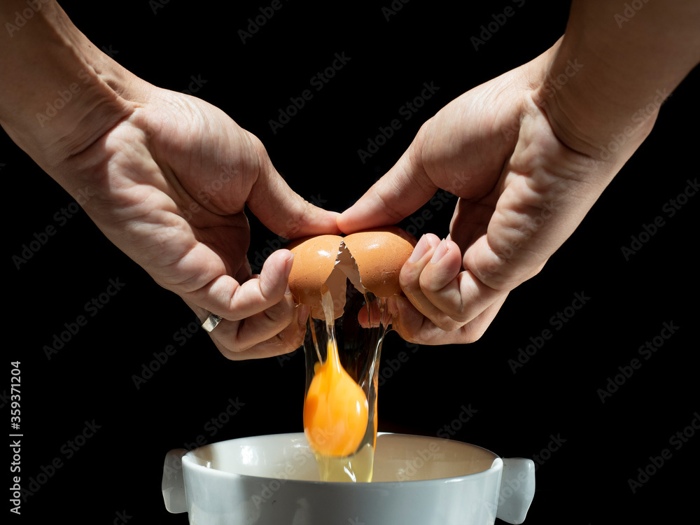 Man hands with ring cracking or breaking an egg into white bowl. egg drop into bowl on black background. Man hands with ring cracking or breaking an egg into white bowl. egg drop into bowl on black background.