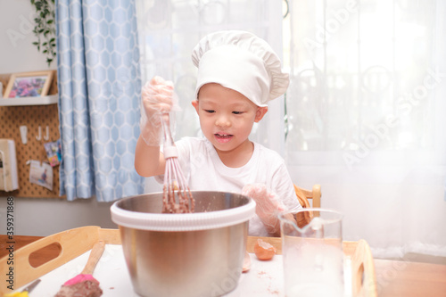 Cute happy smiling Asian 4 years old boy child having fun preparing cake or pancakes enjoy process mixes dough using whisk at home, Cooking with kids, Fun indoor activities for kindergarten concept