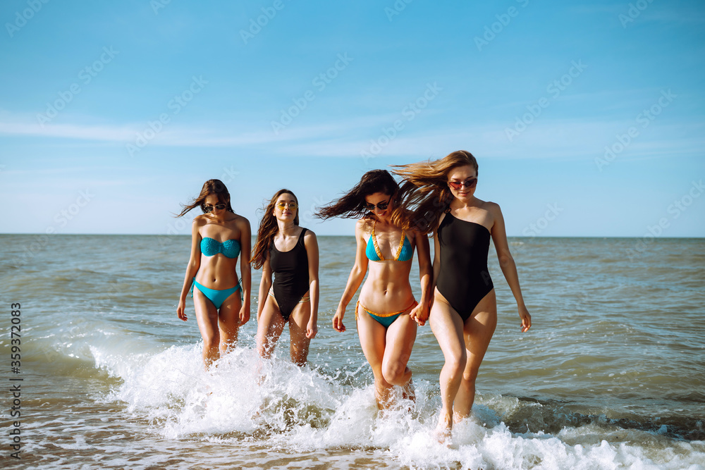 Group of happy young women walking on a beach. Four female friends strolling along the sea shore on a summer day, enjoying vacation. Group of happy young women walking on a beach. Four female friends strolling along the sea shore on a summer day, enjoying vacation.
