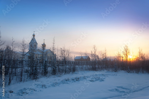 Beautiful early morning winter landscape with colorful gradient sky, sunrise, trees covered in snow and orthodox church on the horizon in Khandyga, Yakutia Sakha Republic, Russia