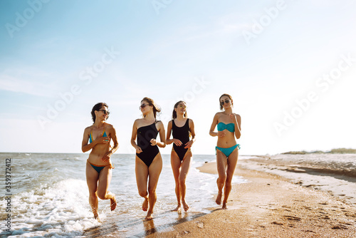 Group of happy young women walking on a beach. Four female friends strolling along the sea shore on a summer day, enjoying vacation.
