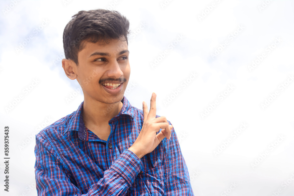 Young teen man showing victory action on sky background. Young teen man showing victory action on sky background.