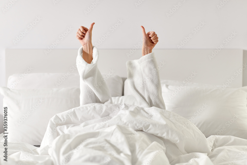 gesture, comfort and morning concept - hands of young woman in hotel robe lying in bed and showing thumbs up at bedroom - obrazy, fototapety, plakaty 