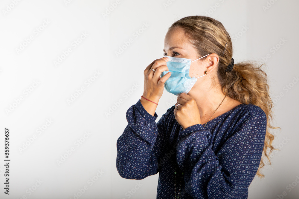 woman with blue shirt in medical mask fixing the mask on the nose in front of white wall. woman with blue shirt in medical mask fixing the mask on the nose in front of white wall.