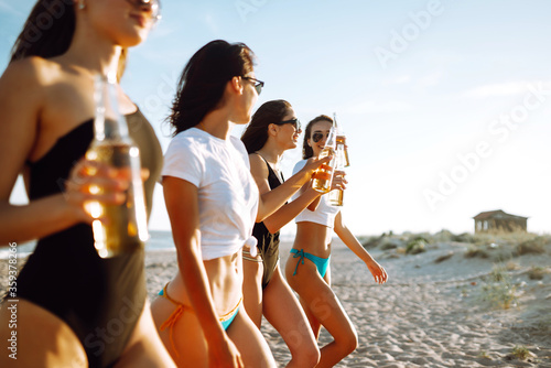 Four beautiful girls cheers and drink beers on the beach, enjoying vacation. Vacation time laughing and smiling. © maxbelchenko