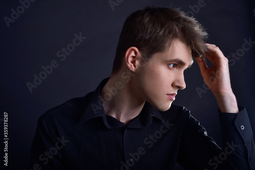 Studio portrait of a guy in a black shirt on a black background. A handsome young guy of European appearance. The guy cares for himself, touches his hair, haircuts and gels for men's hair