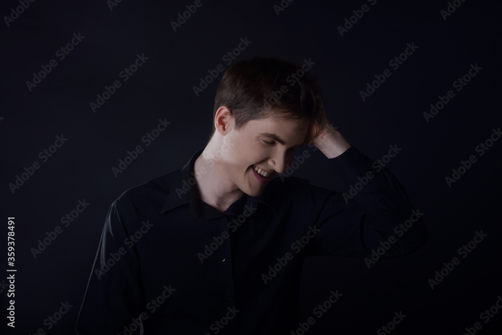 Studio portrait of a guy in a black shirt on a black background. A handsome young guy of European appearance. The guy laughs, the guy in a good mood looks at the camera