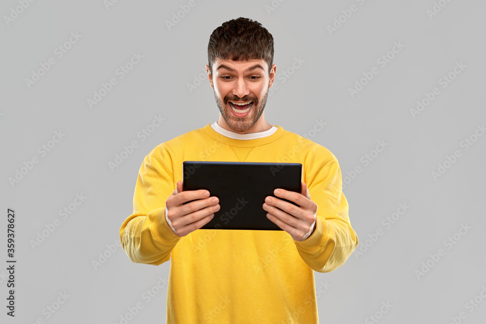 technology and people concept - smiling young man in yellow sweatshirt with tablet pc computer over grey background technology and people concept - smiling young man in yellow sweatshirt with tablet pc computer over grey background