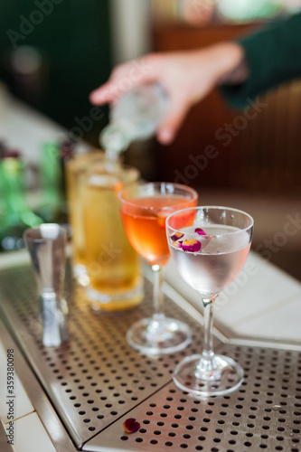 Several beautiful cocktails at the bar, bartender adding soda to one of them on the background