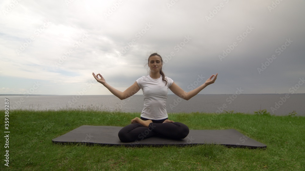 Young fit woman practice yoga on coast near the lake or sea. Woman sitting in Knee Pile pose and meditating Young fit woman practice yoga on coast near the lake or sea. Woman sitting in Knee Pile pose and meditating