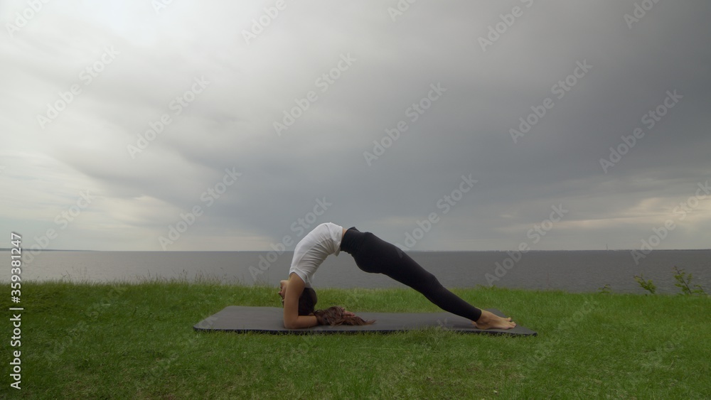Fototapeta premium Young fit woman practice yoga on coast near the lake or sea. Woman doing Inverted Staff Dvi Pada Viparita Dandasana pose