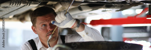 Close-up of mechanic checking oil level in car engine. Automobile on mechanical lift. Special equipment for diagnostic. Service station and machine maintenance concept