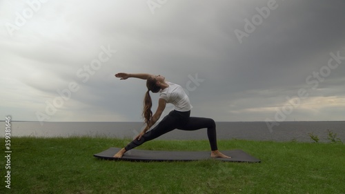 Young fit woman practice yoga on coast near the lake or sea. Woman doing Reverse Warrior Pose