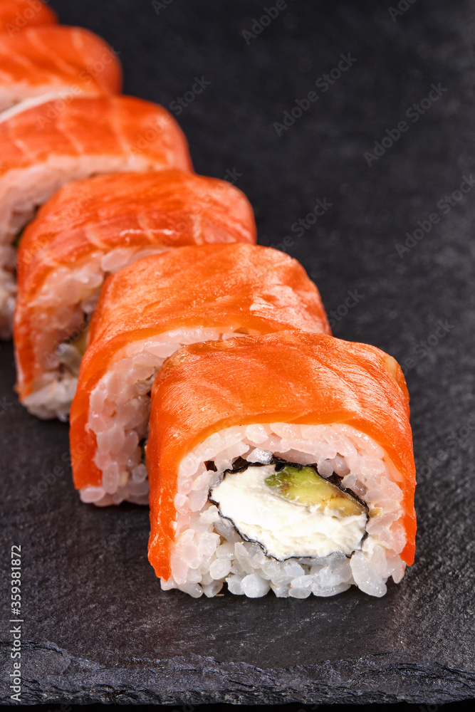Beautiful sushi roll topped with salmon stuffed with cream cheese on a black stone board. Beautiful sushi roll topped with salmon stuffed with cream cheese on a black stone board.