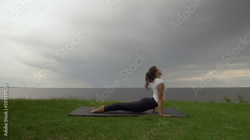 Young fit woman practice yoga on coast near the lake or sea. Woman doing High Cobra Pose