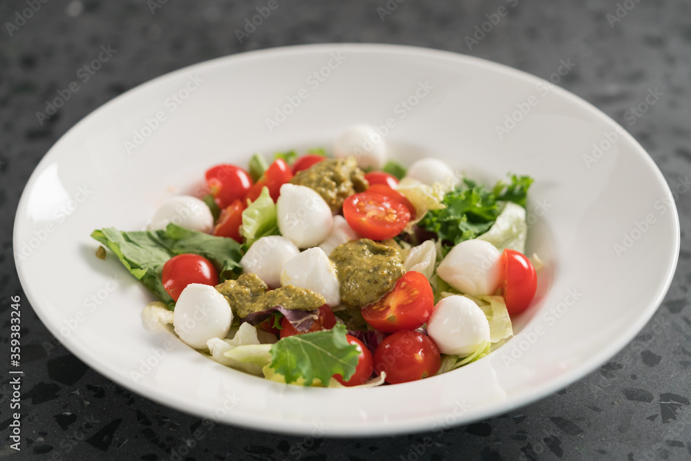 Salad with miced greens , tomatoes and mozzarella in white bowl